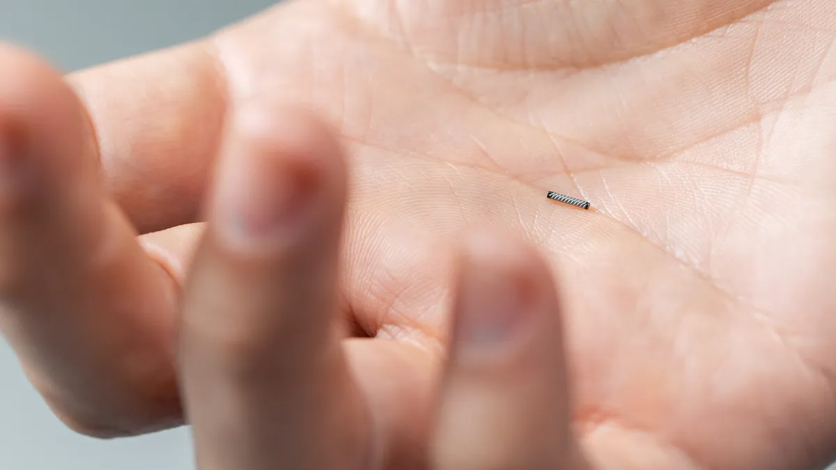 Close up of a person holding a small, cylindrical device in the palm of their hand.