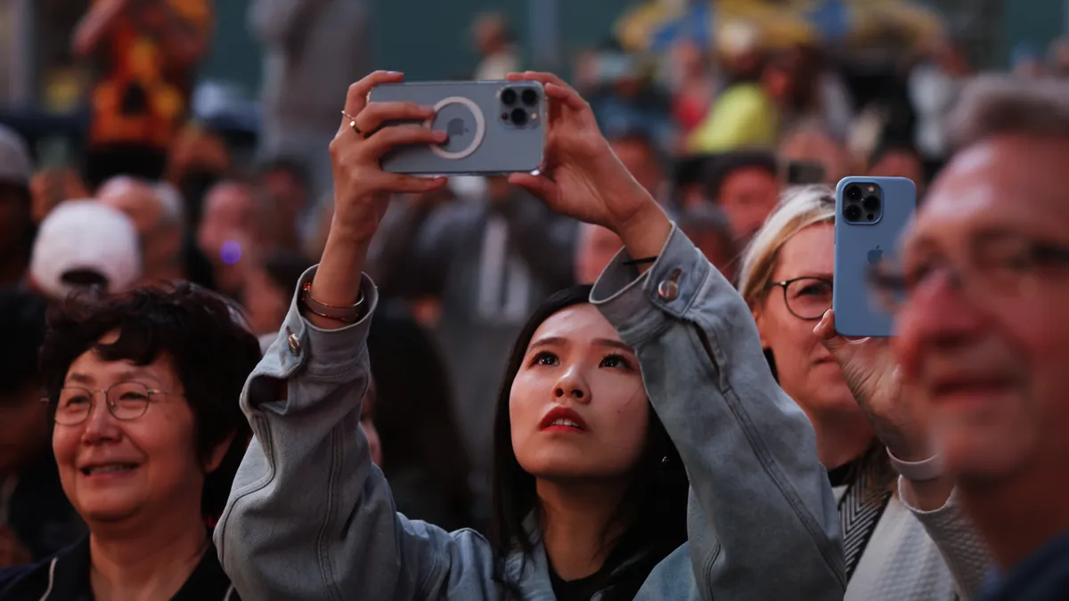 A woman in a crowd holds a phone camera above her head.