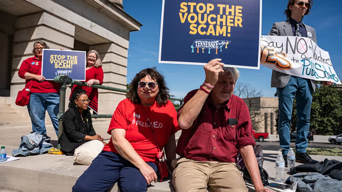 People are gathered outside a building holding signs protesting school vouchers.