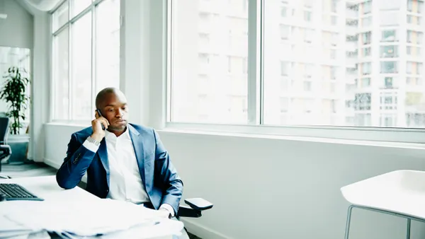 Frustrated businessman sitting at office workstation waiting while on smartphone