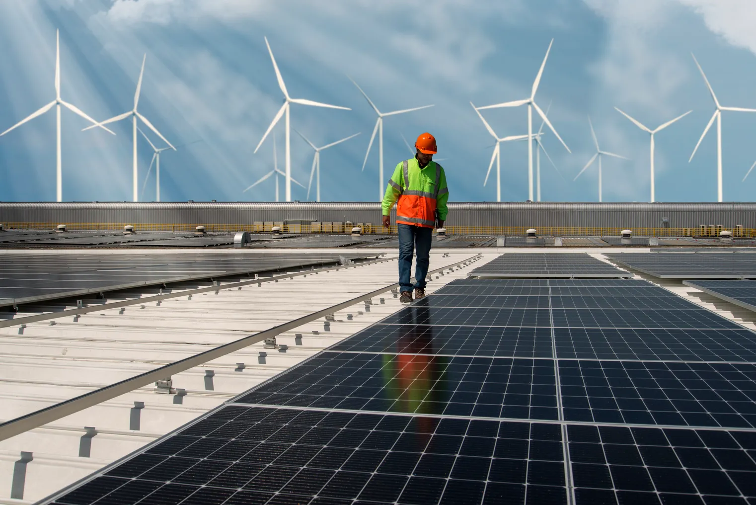 An engineer walks by solar panels with wind turbines in the background.