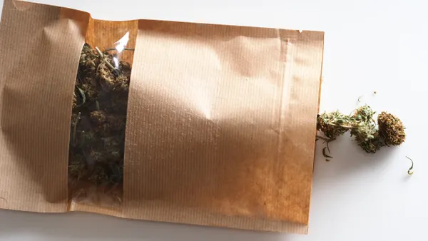 A pouch with a transparent window houses cannabis flower.