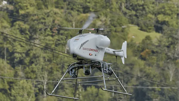 A drone that resembles a helicopter is seen hovering in front of power lines and trees.