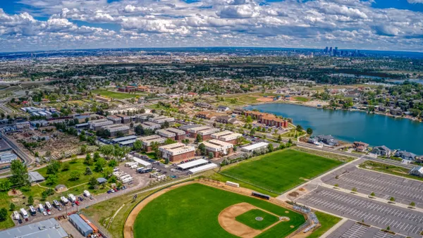 Aerial view of city with baseball field in the foreground, lake and mountains on the horizon.