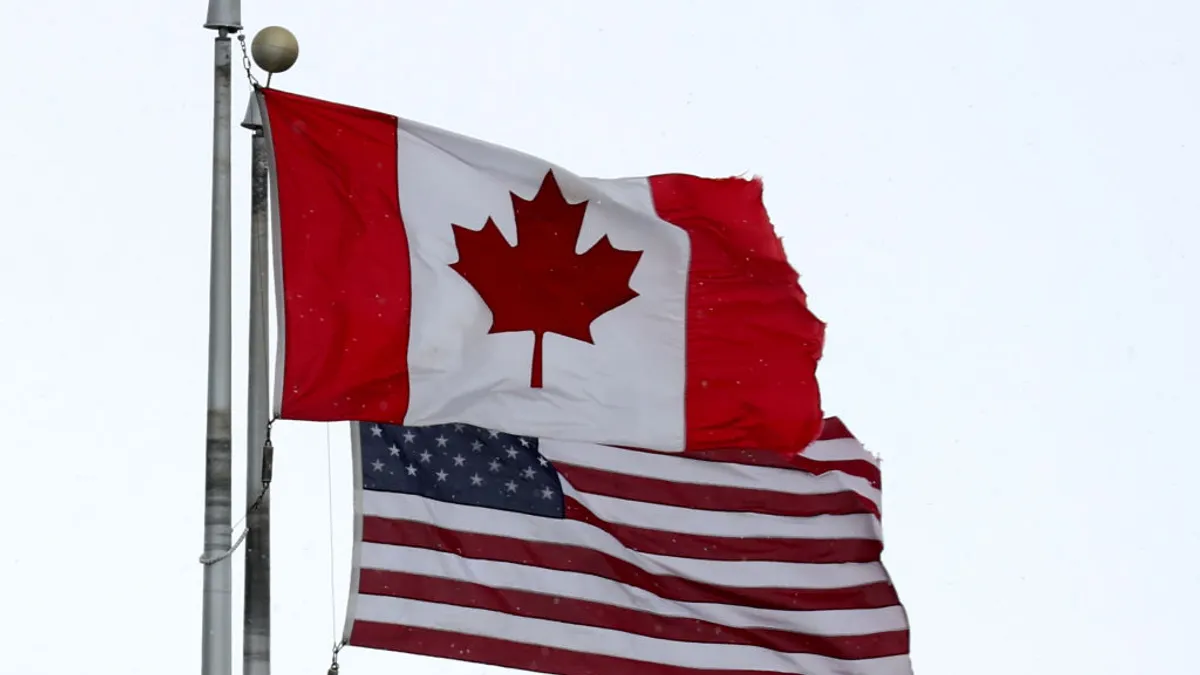 A Canadian flag next to an American flag next to each other waving in the air.