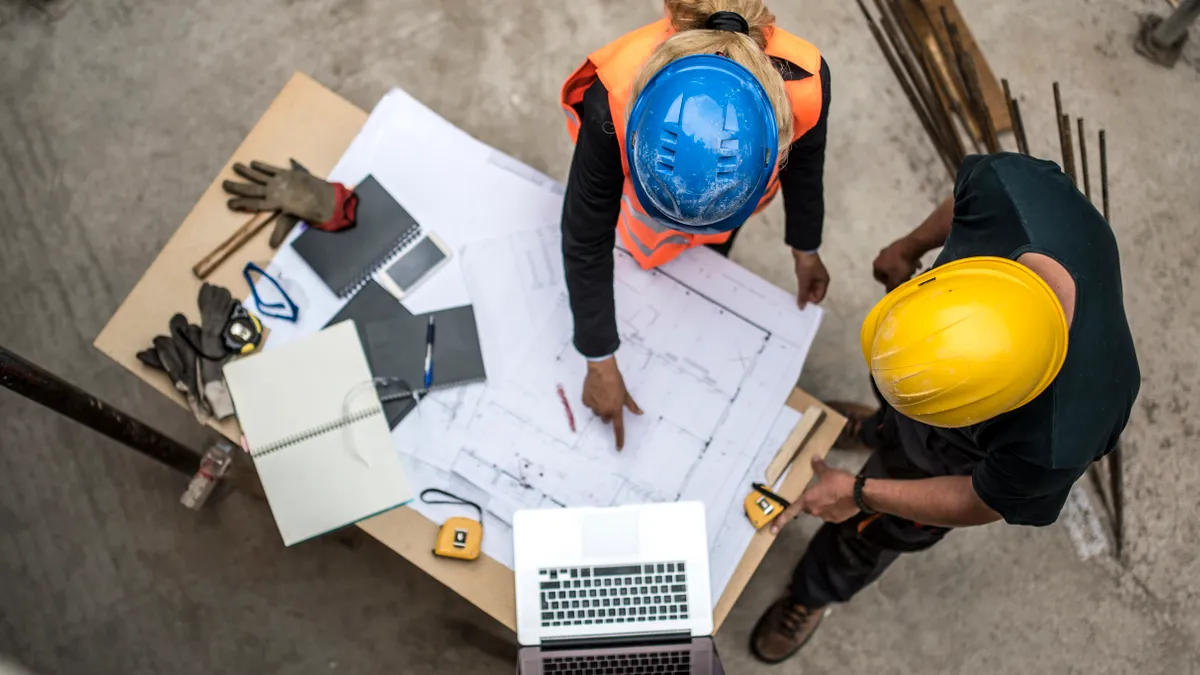 An overhead view of two people in construction gear looking over plans on a table.