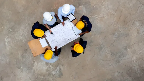 A group of people in safety vests and hard hats looking at a blueprint from a top down view
