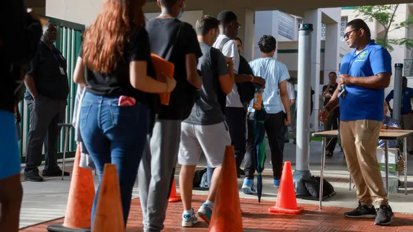 Students are seen from behind as they walk through a weapons detection system outside a school building.