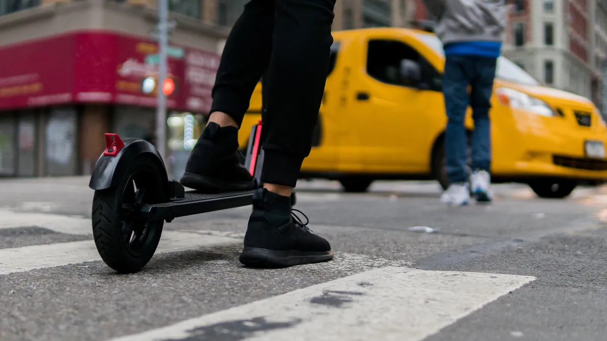 Close-up of person's feet on electric scooter, with a yellow car in the background