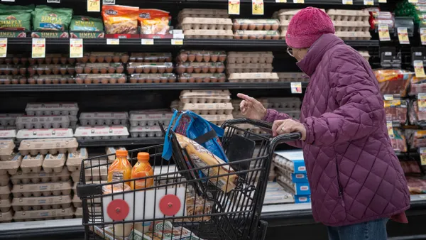 A shopper in a pink coat stands with her cart and considers the egg selection.