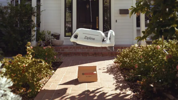 A photograph of a small drone-like device lowering a bag with a Chipotle logo on it to the ground.