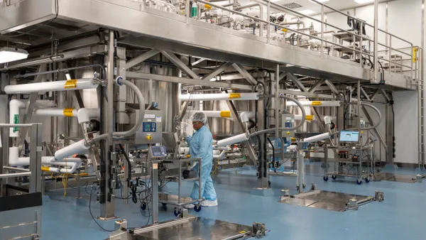 A woman in scrubs standing next to manufacturing equipment in a large room filled with scientific steel equipment