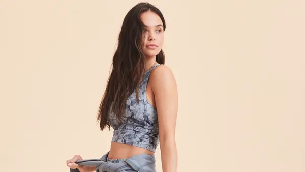 A person in activewear ties a grey sweater around their waist.