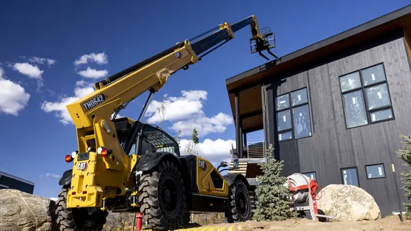 Caterpillar's compact telehandler raises its industrial arm above a house during a construction project.