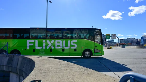 A large green motor coach crossing an intersection under a deep blue sky.