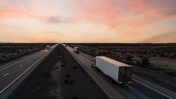 Aerial drone shot showing a vibrant sunrise in a desert area with trucks going both ways on a highway.