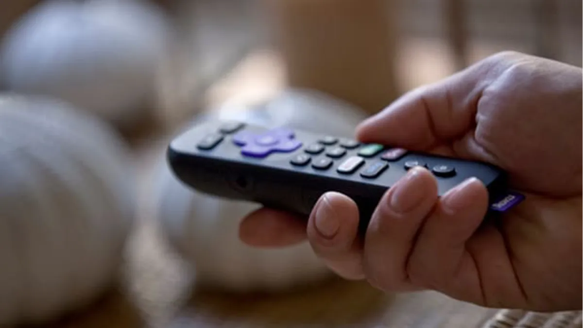 A hand holds a TV remote control