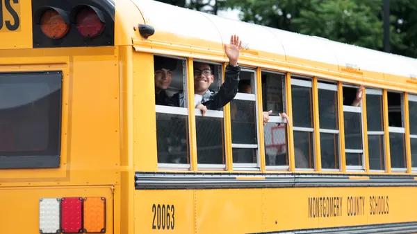 A waving student leans out of a school bus