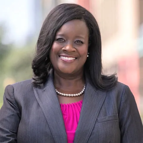 Woman in gray blazer and pink shirt smiling into camera.