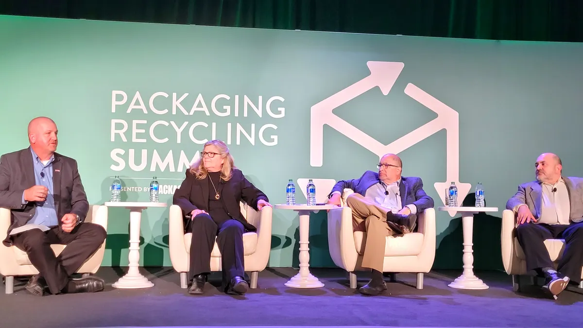 Four people sit in chairs on a stage with a green background that says "Packaging Recycling Summit" in white letters.