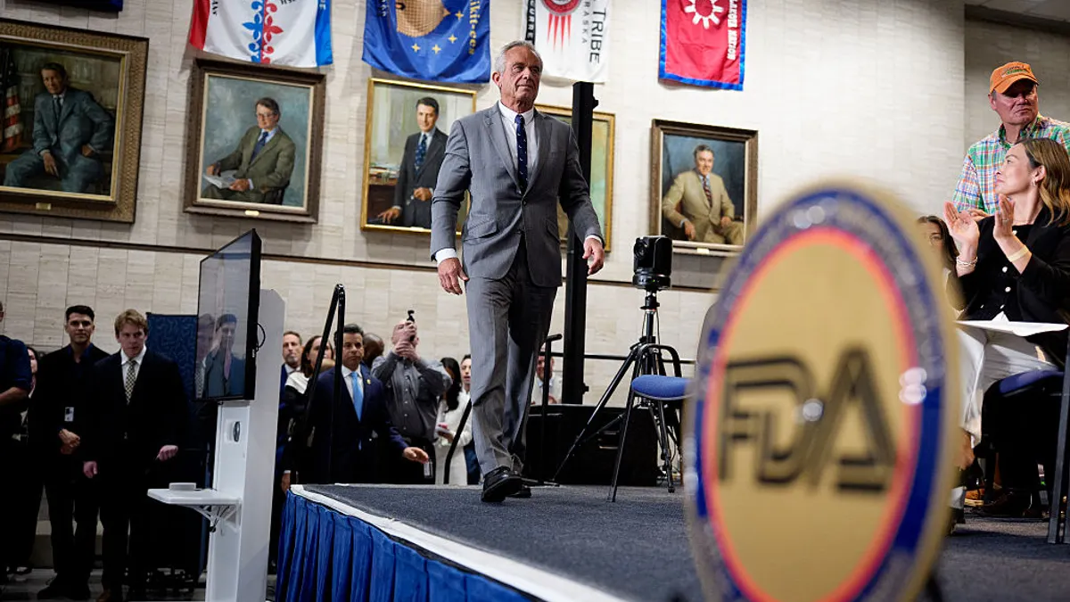 Robert F. Kennedy Jr. walks onto a stage. In the foreground, the FDA logo can be seen