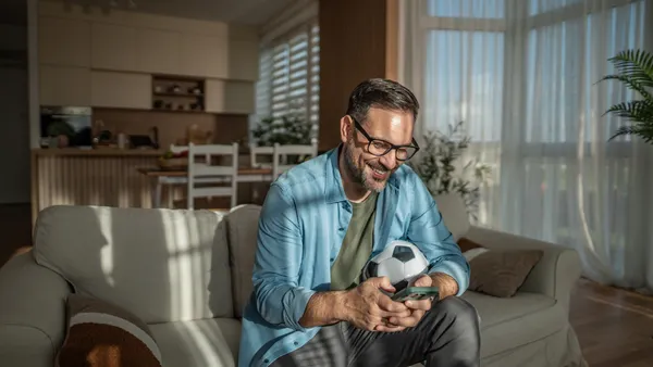 A man holding a soccer ball checks his phone.