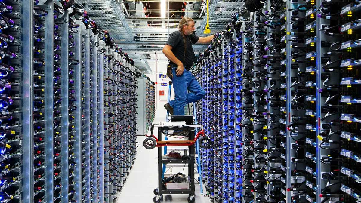 A man stands on a cart in an corridor between computer servers.