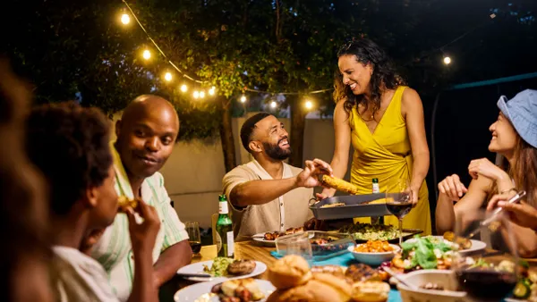 Family and friends dining at an outdoor table under string lights by the pool. Evening social gathering with food and drinks. Summer celebration concept.