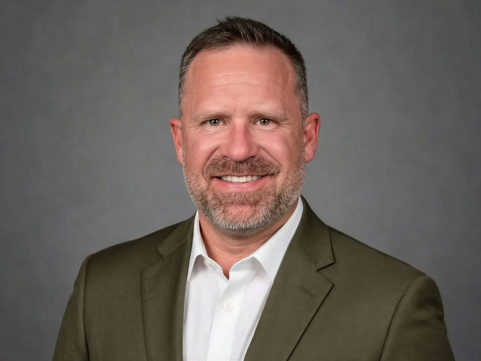 A headshot of a person wearing a suit and white shirt in front of a grey background