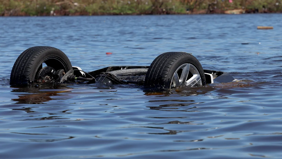 An upside-down vehicle is submerged in blue water with just two wheels showing.