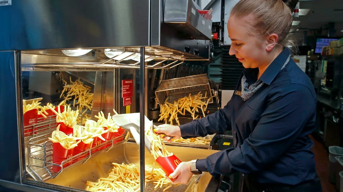 A woman at a frying station putting french fries in bags.