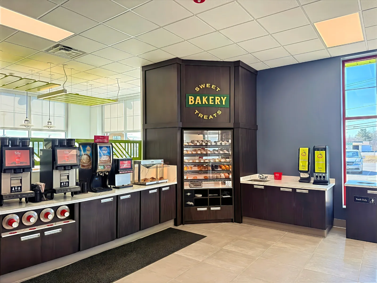 A beverage and bakery area inside a store. A sign over the bakery shelves says Sweet Treats Bakery