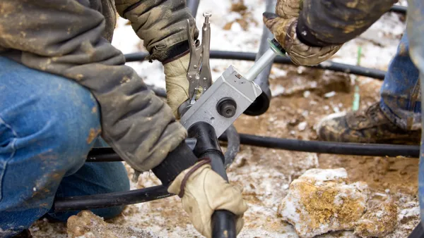 Closeup of the hands of two people holding together pipes. One pair of hands holds a tool.