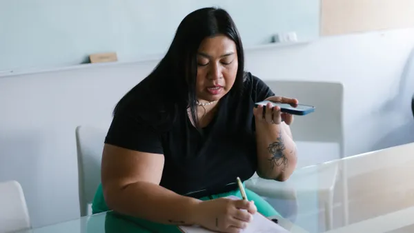 A person writes on papers on a clipboard while using speakerphone.