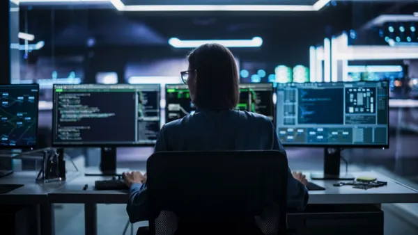 woman sitting in front of several computer screens during cybersecurity training.