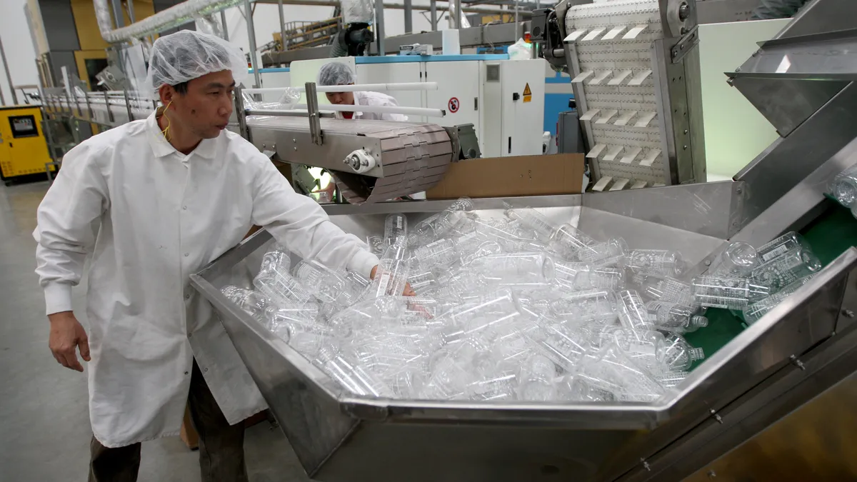 A worker grabs an empty bottle out of a bin