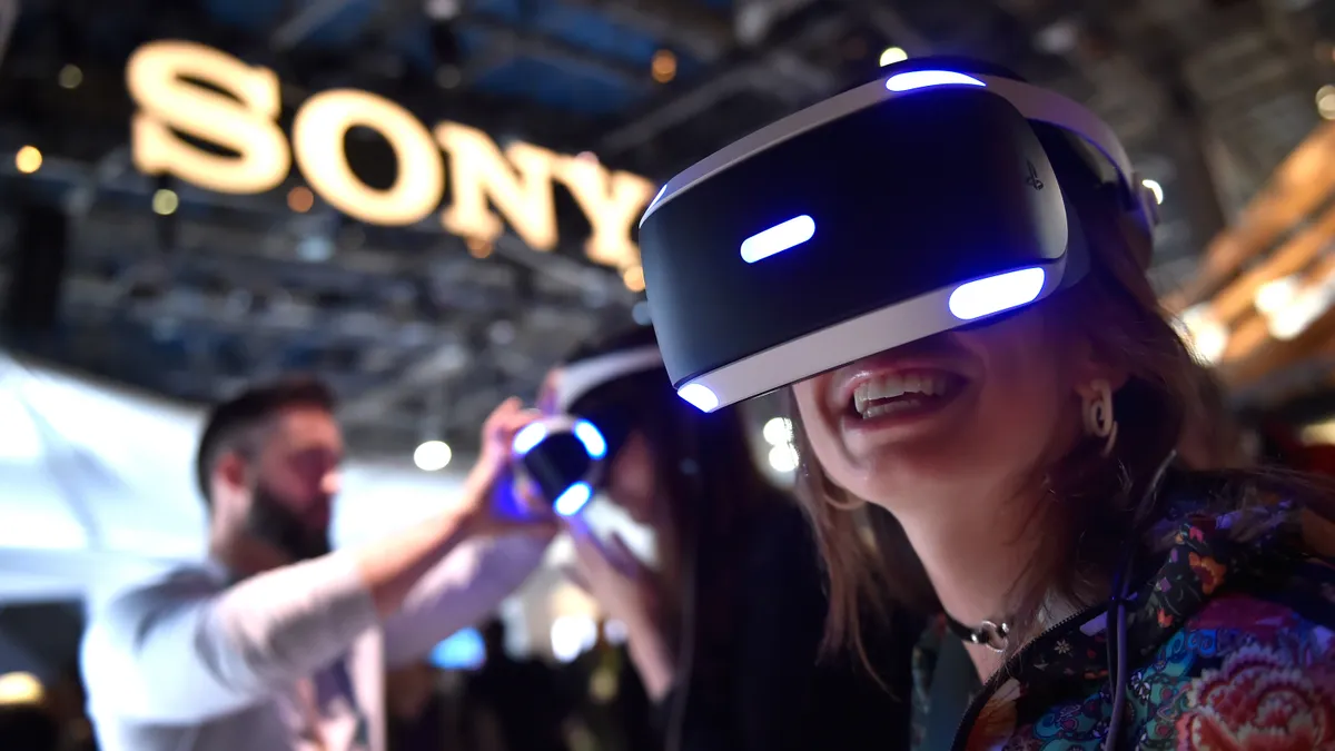 Two people try on virtual reality headsets in a location with a large sign that reads: "Sony."