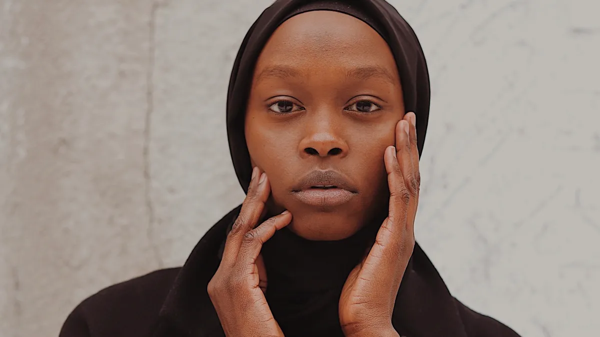 A feminine-presenting Black person wears a hijab