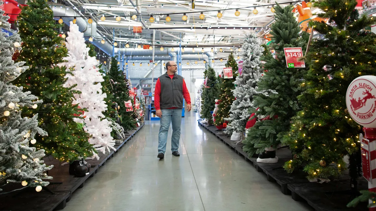 A customer walks through an aisle of artificial Christmas trees in a Walmart store.