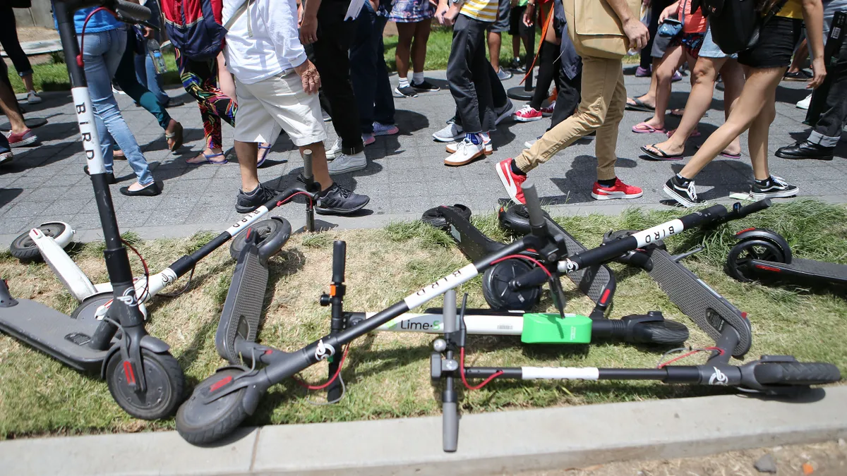 A photo of several e-scooters lying along a sidewalk.