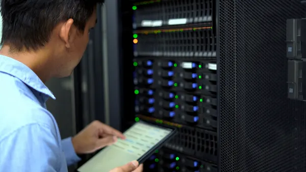 An IT technician inspects and manages a server rack in a data center using a tablet.