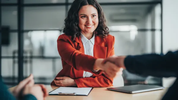 A woman in a blazer shakes hands in the office