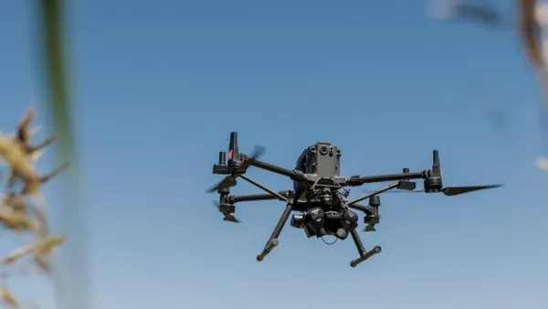 A Sentera drone flying in the air over a field.