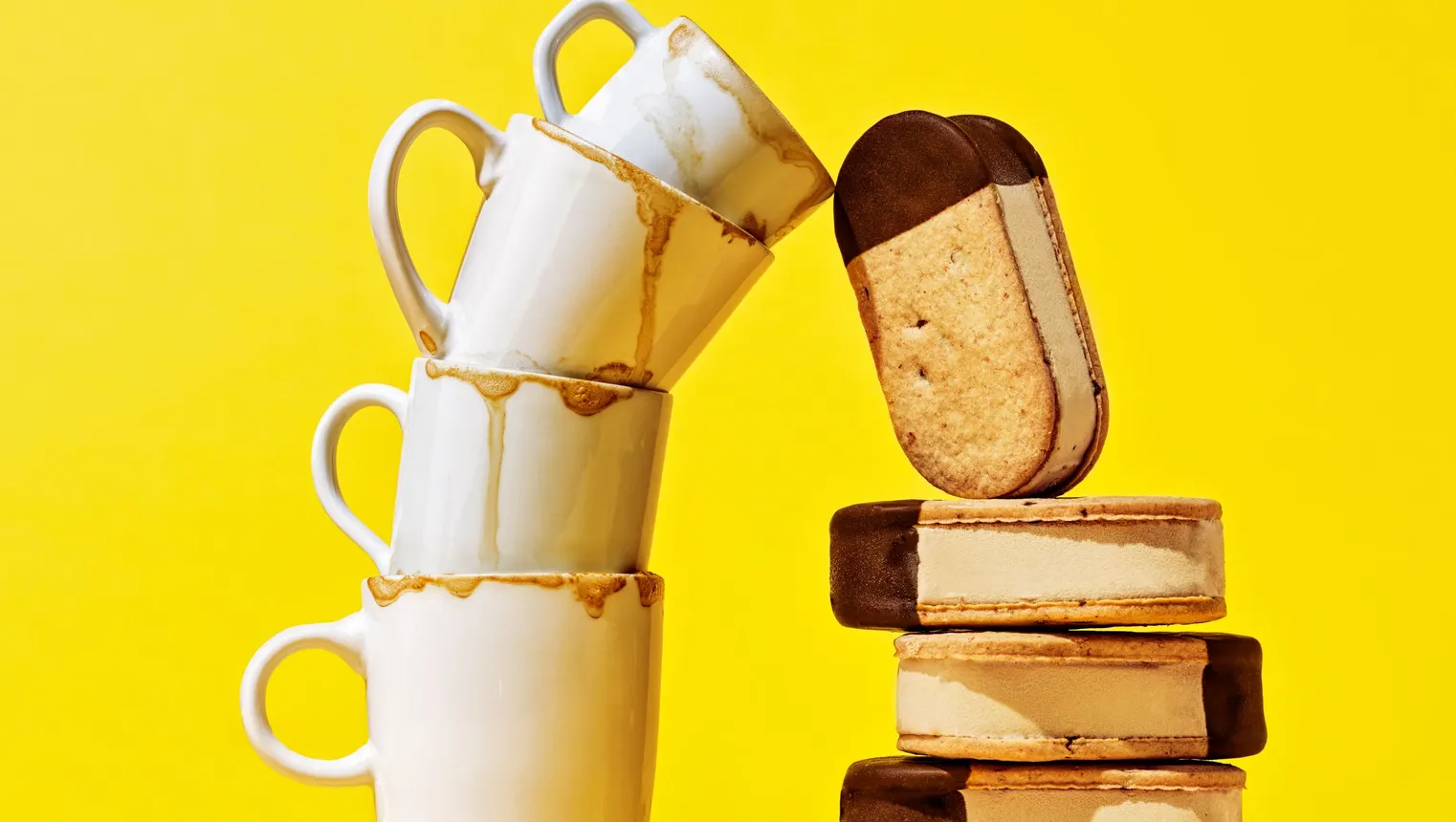 Four gelato ice cream sandwiches are stacked next to four coffee cups.