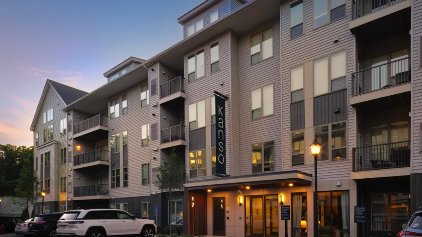 Tan, garden-style apartment with Kanso sign and cars in front.