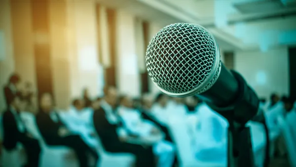 A microphone sits against a blurred background with people sitting down.