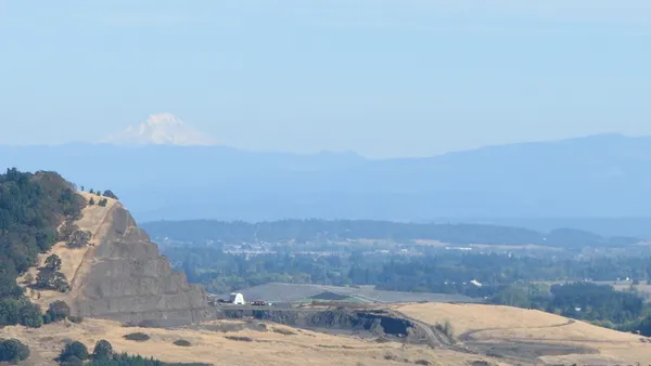 View of a stepped butte in foreground on left of image with landfill rising behind it and a snow-capped mountain in the background