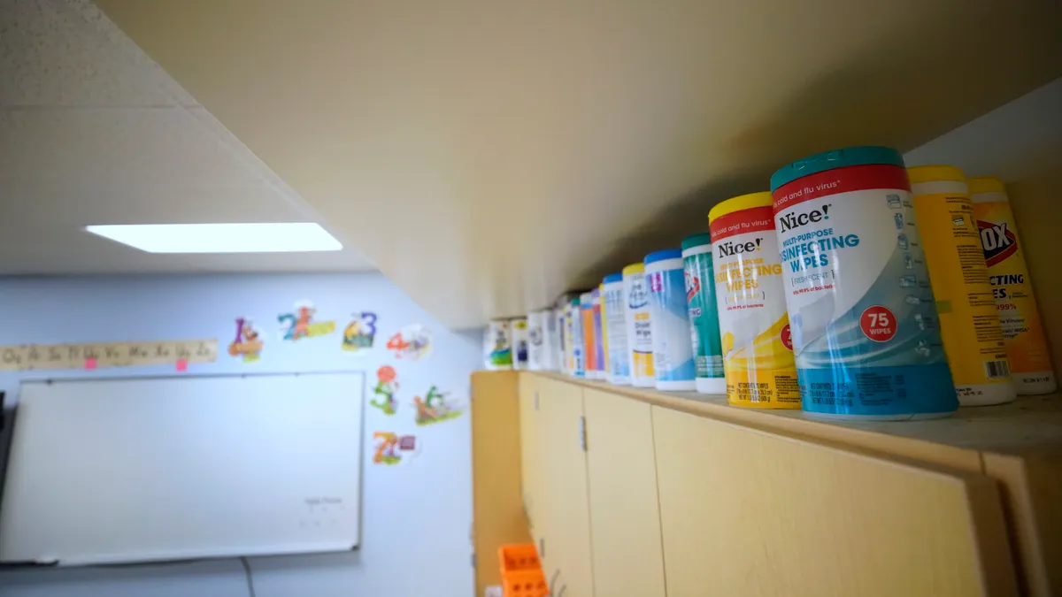 Canisters of cleaning wipes sit on the top of a cabinet in a classroom.