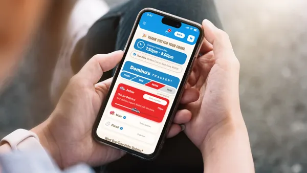 A person holds a smartphone that shows tracking information for a delivery order from Domino's