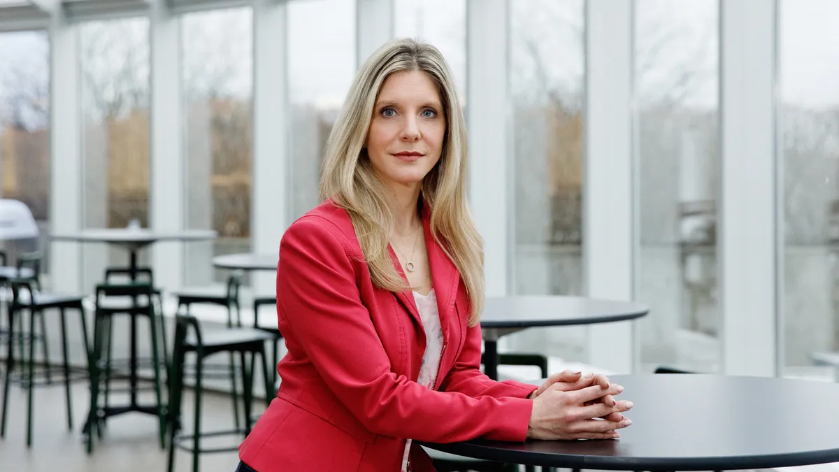 A blonde woman in a red blazer stands at a table